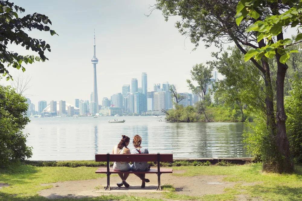 Two girls sitting on a park bench by a lake overlooking downtown in Toronto, one of the best places to visit in September