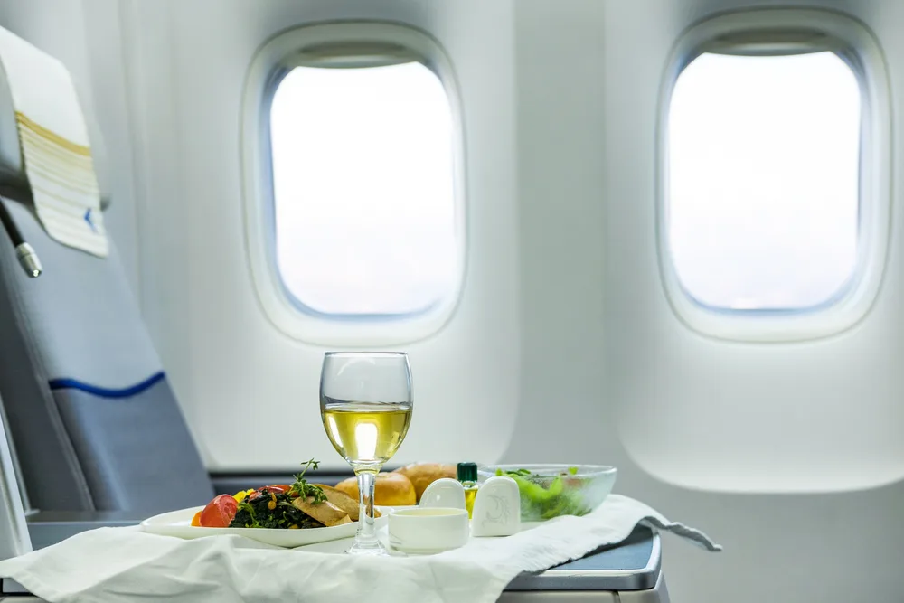 Business class seat on an airplane with wine glass and dinner on the table in front of a window for a piece on business class vs. first class seating