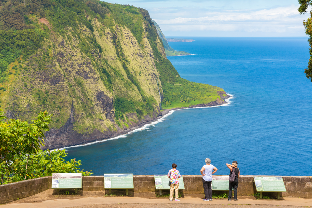 Group of three tourists soaking in the natural beauty of the Waipio Valley lookout on the Big Island