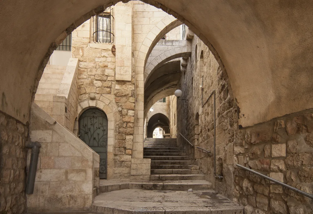 Old hidden city passageway pictured during the least busy time to visit Jerusalem with stone walls on either side and gorgeous arches above steps with nobody around