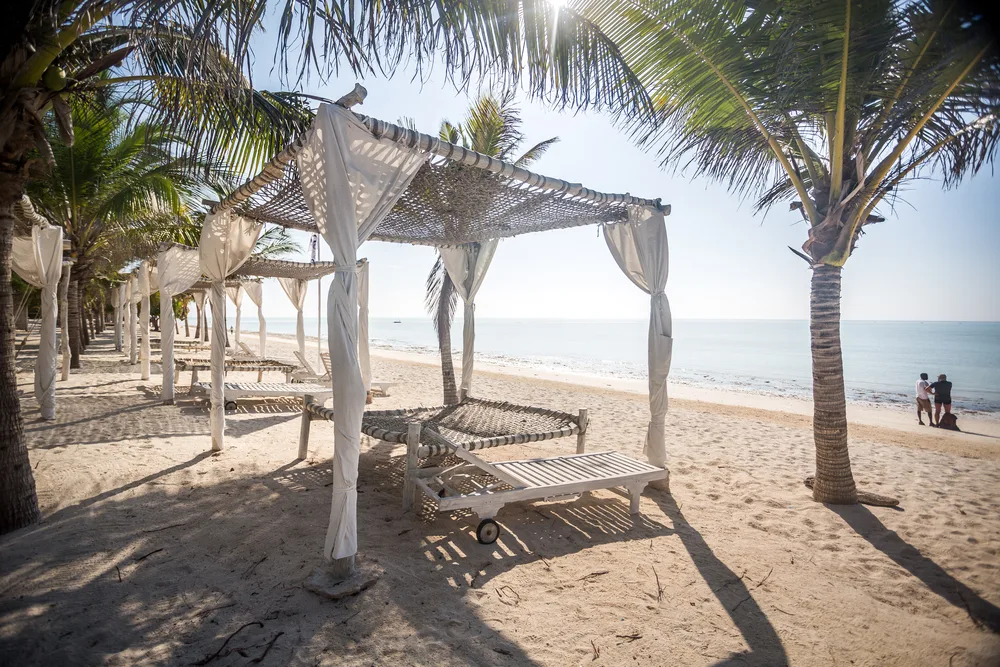 Watamu Beach is one of the best beaches in Africa, shown with a canopy and beach chairs overlooking the waves and blue skies with palm trees
