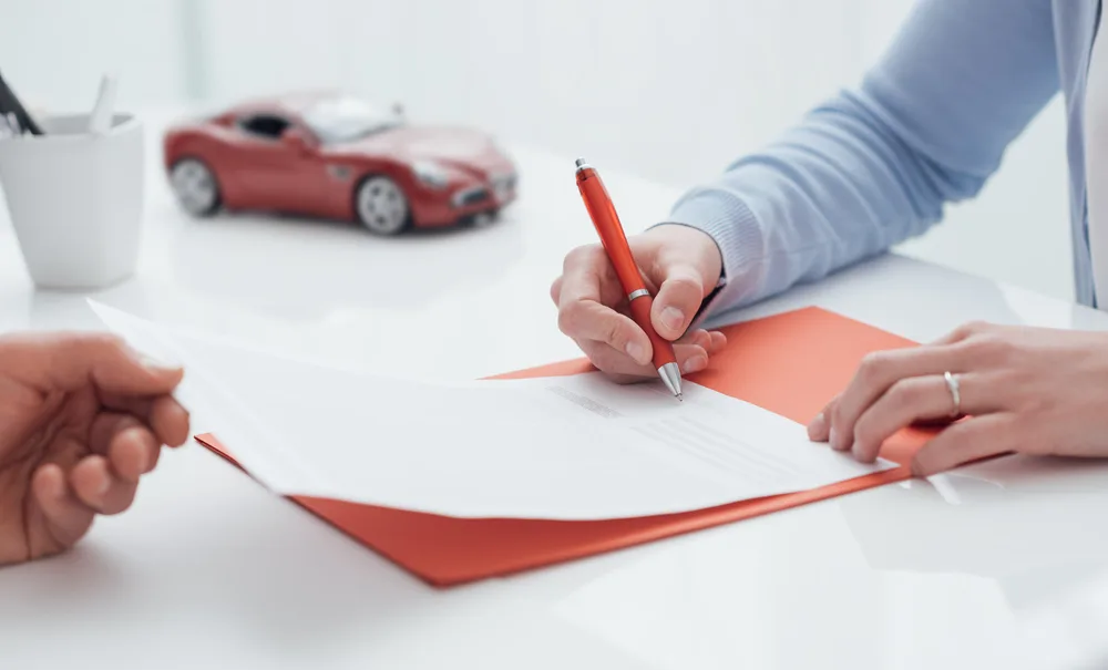 Woman signs rental car insurance form on orange clipboard for a piece explaining how to rent a car without a credit card