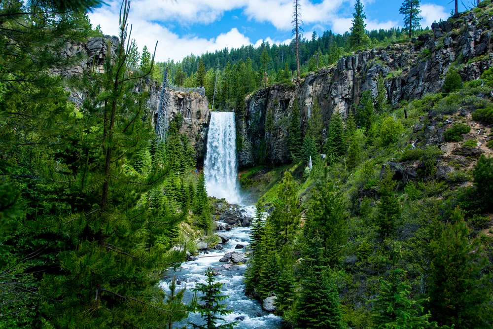 Tumalo Falls pictured during the best time to visit Bend, Oregon with a gorgeous waterfall as seen from the middle of a couple trees
