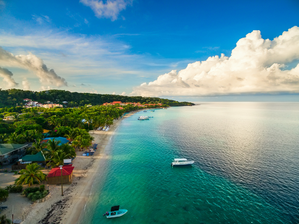 Aerial image of a beach in Roatan pictured during the best time to visit Honduras with a few clouds over still water