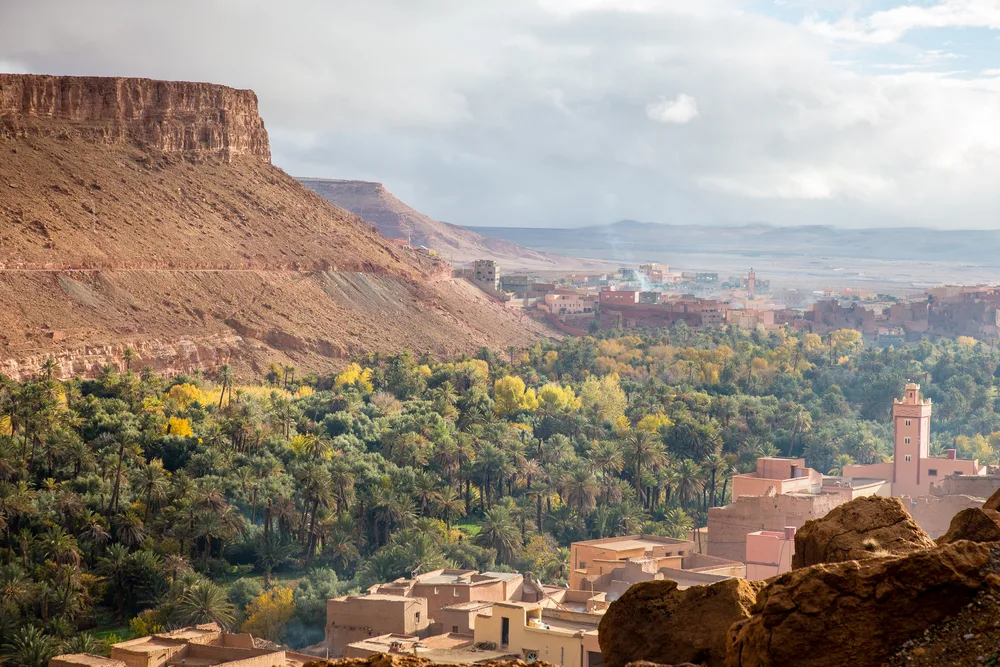 Cliffside view of Draa Valley, one of the best places to visit in Morocco, pictured with the tan, mud-walled town overlooking the huge rock face and valley below