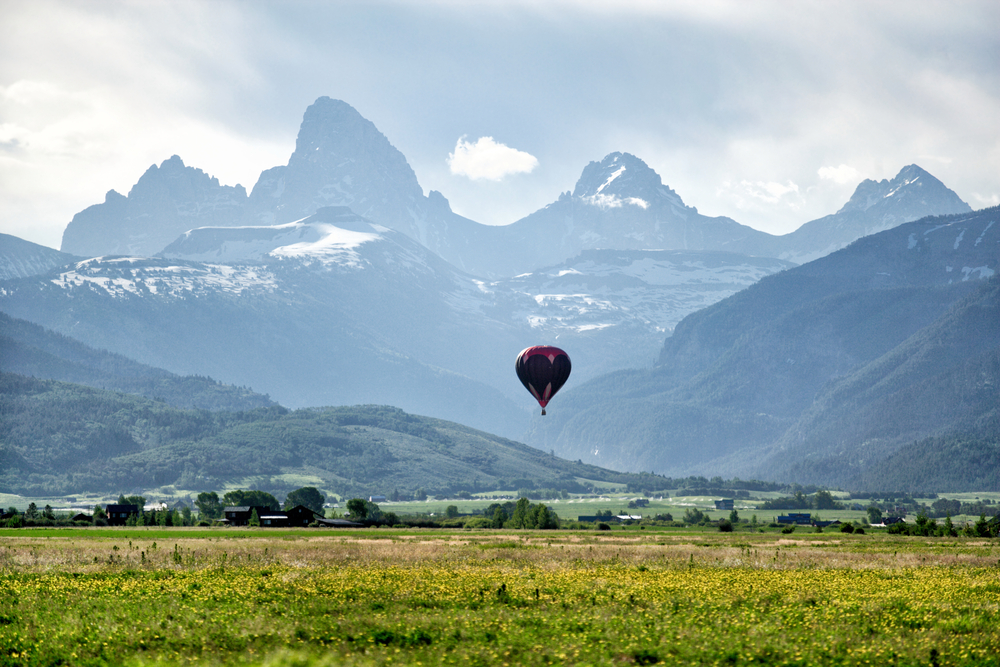 Hot air balloon over a valley in between mountains pictured during the cheapest time to visit Idaho