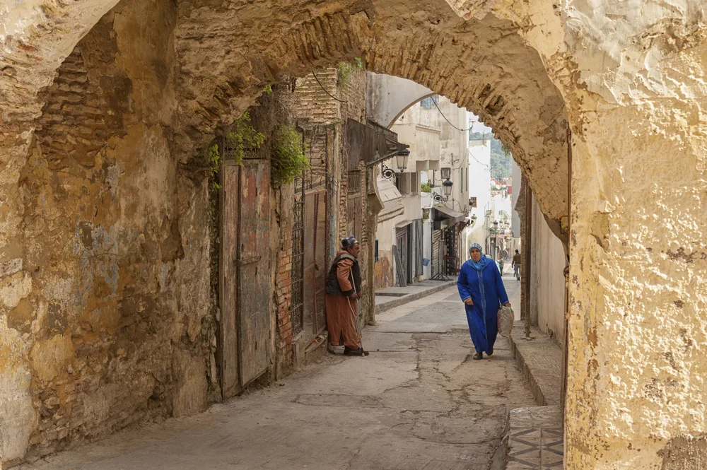 Old stone walls of Meknes, Morocco, pictured with two locals walking along the path between the walls