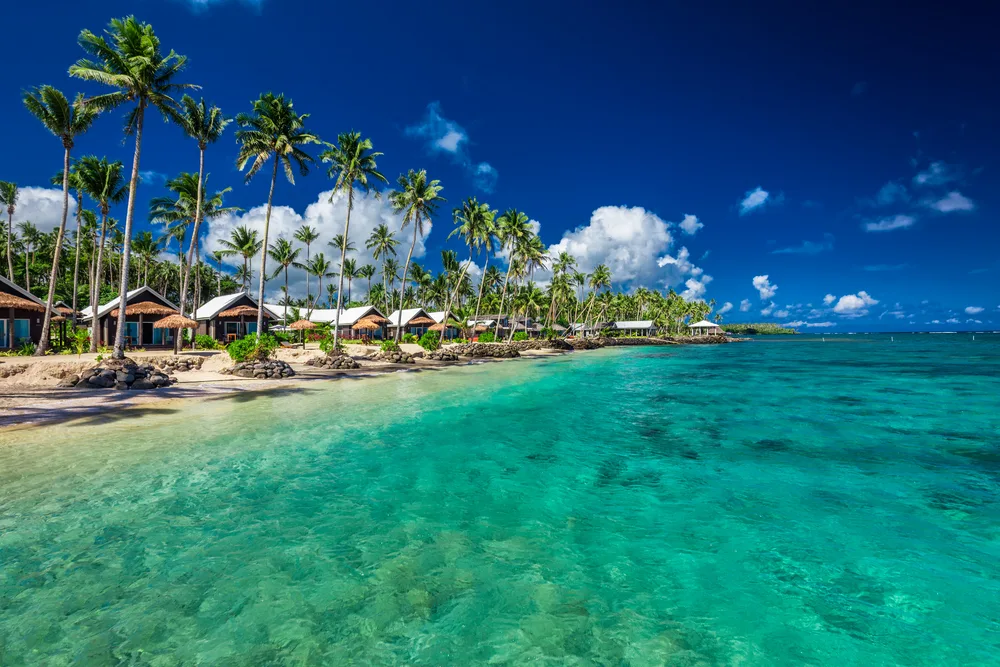 Gorgeous white sand beach with clear teal water and blue skies above pictured during the best time to visit Samoa
