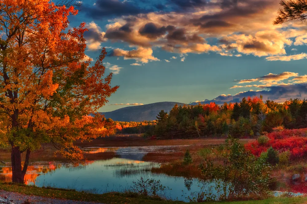 Very picturesque view of Acadia National Park at dusk with still water reflecting the scene of the mountain and trees while clouds linger overhead as one of the best places to visit in October