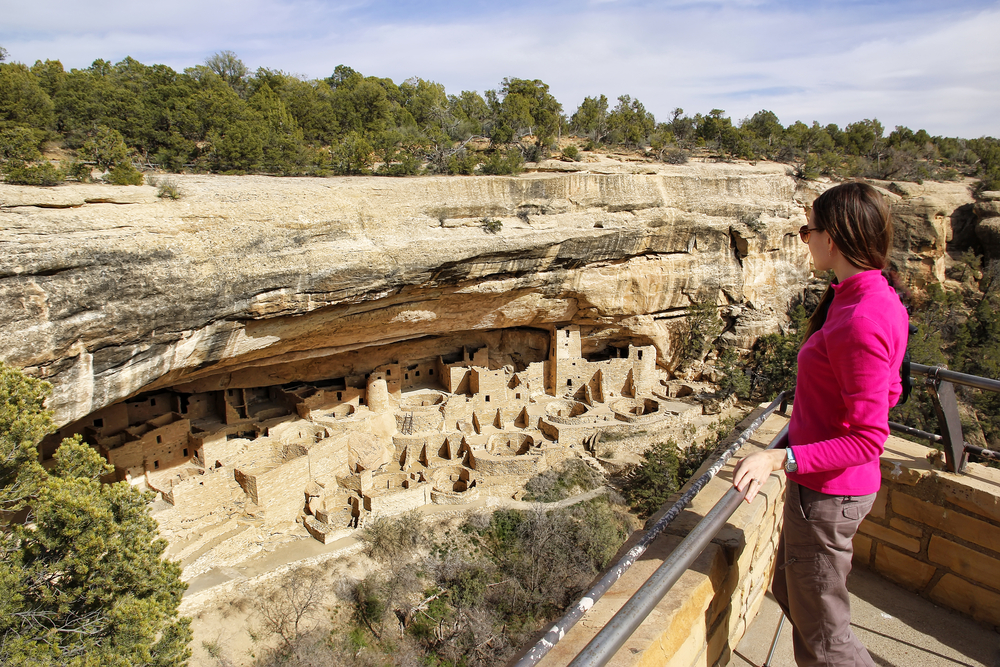 Tourist in a pink shirt stands at the edge of an overlook point looking down at the cliff dwellings below during the least busy time to visit Mesa Verde National Park