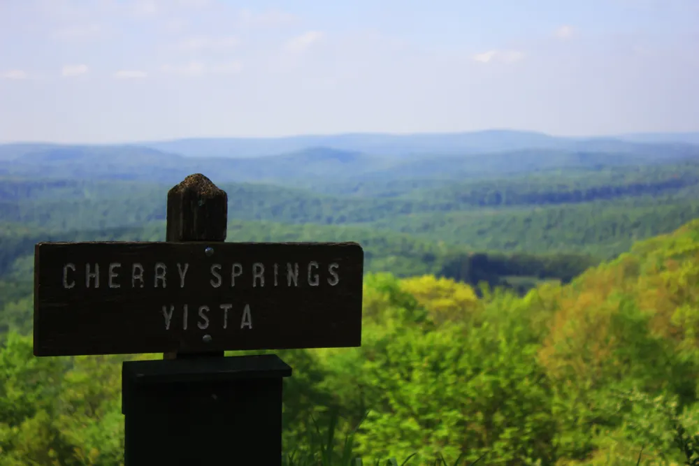 Sign that says Cherry Springs Vista pictured overlooking a treed ridge during the best time to go to Cherry Springs Park in Pennsylvania
