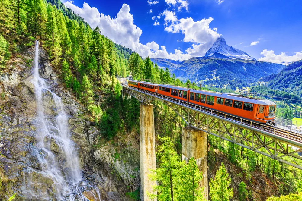 Zermatt, Switzerland, pictured with the red train going above a gorge next to a waterfall