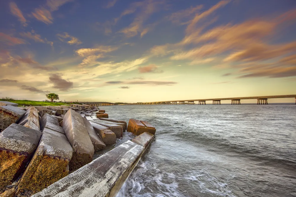 Old concrete pier collapsed and lying in the water with the sun setting over the bridge pictured during the best time to visit Amelia Island