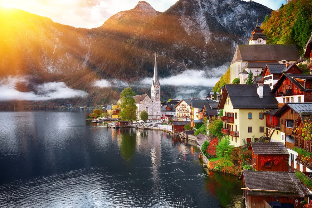 Hallstatt Austria, a top pick for the best places to go to in October, pictured with the sun reflecting on the water and overlooking the charming little town