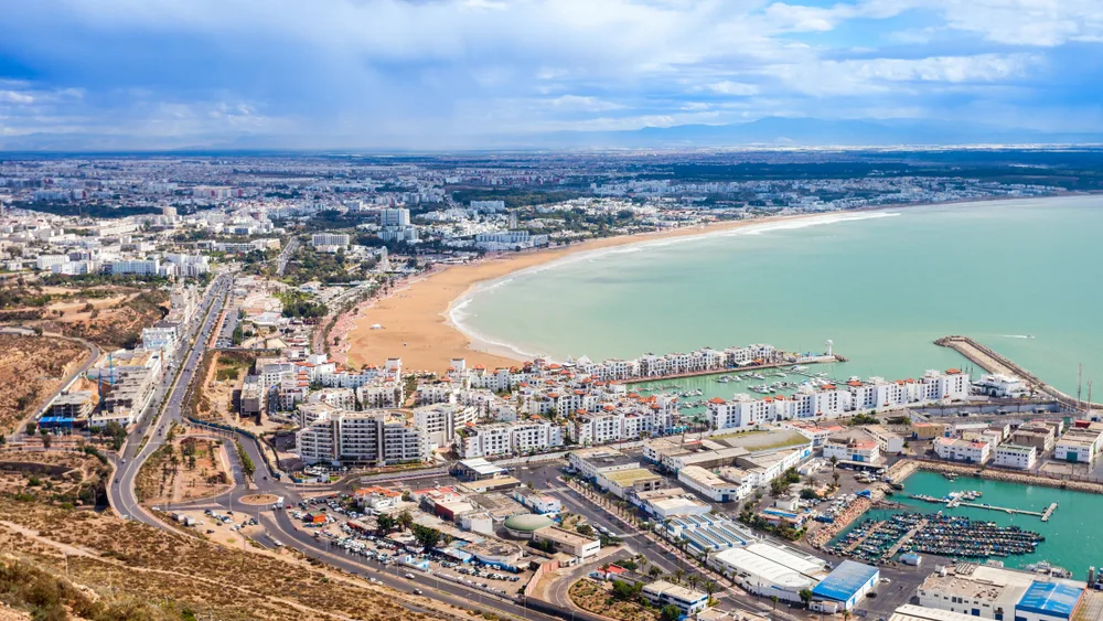 Panoramic view of Agadir, with its expansive beach surrounded by resorts and buildings, as seen from the air on a calm day