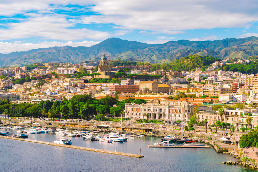 Hillside view of Messina, a top pick for places to visit in Sicily, with boats in the harbor and the homes and buildings overlooking them