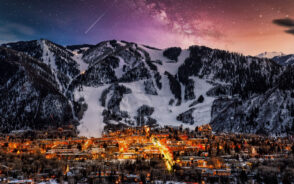 Aspen, one of the best ski resorts in Colorado, pictured at night with a multi-colored sky over the snow-capped mountains