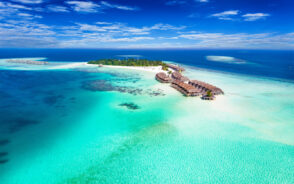 Aerial view of one of the best islands in the Maldives to visit with clear blue and turquoise water and villas on stilts over the ocean