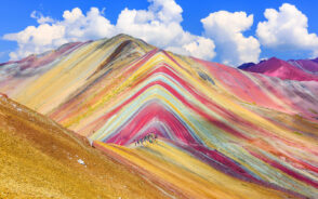 People on the breathtaking multi-colored hills of the Montana de Siete Colores, or Rainbow Mountain, with a blue sky above