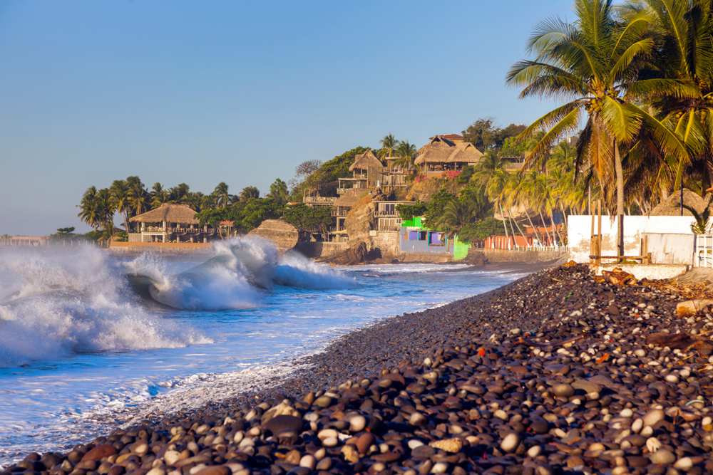 Black rock beach with villas overlooking the ocean above the water in the bay of El Tunco, one of the must-visit places in El Salvador