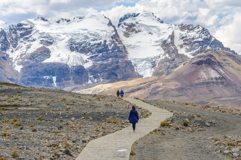Three people walking along a cement path in Huascaran National Park with the enormous glacier dwarfing them