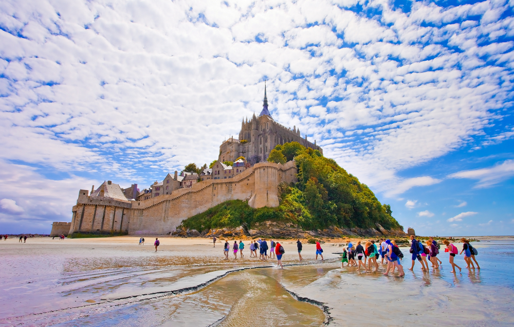 Picture of people walking toward Mont Staint-Michel in Brittany, France, for a piece on the best places to visit in the country, seen at low tide