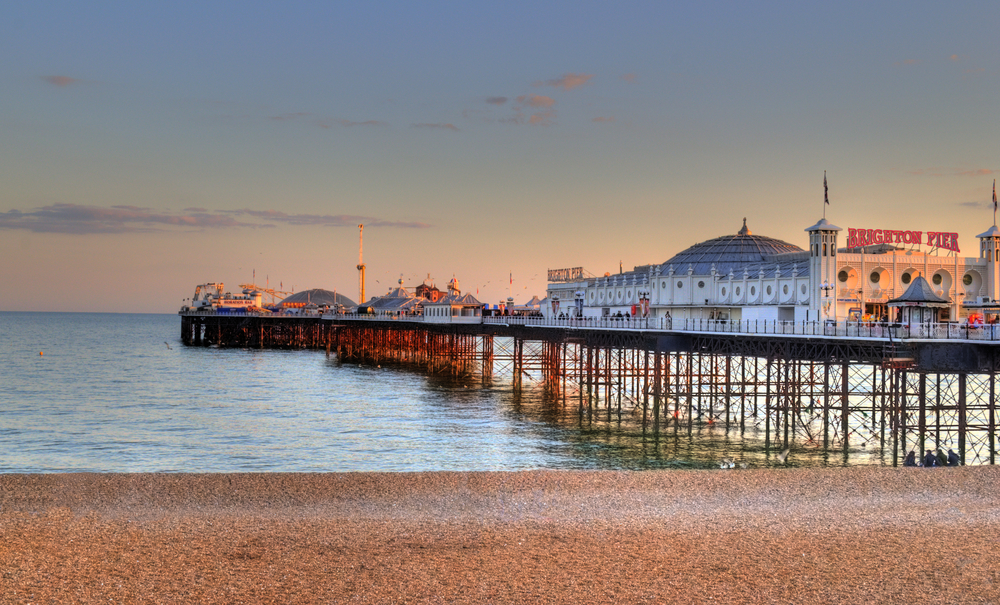 The famous pier in Brighton seen on a still evening day with the sun setting over the horizon, as seen from the beach