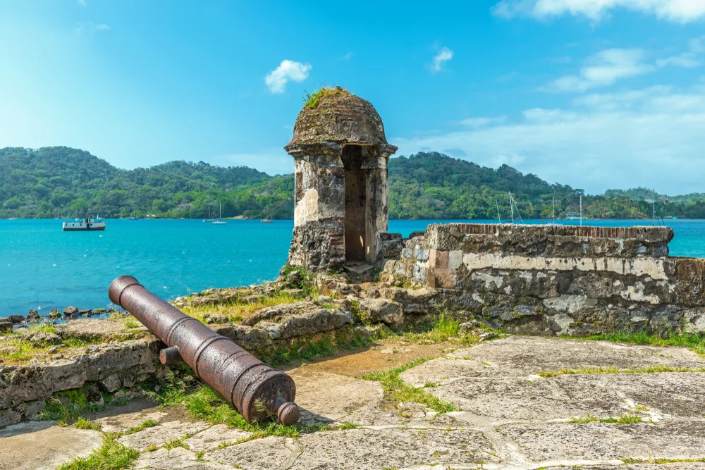 For a roundup of the best places to visit in Panama, a photo of a cannon on the coast of the old ruins in the town of Portobelo overlooking the teal water of the ocean