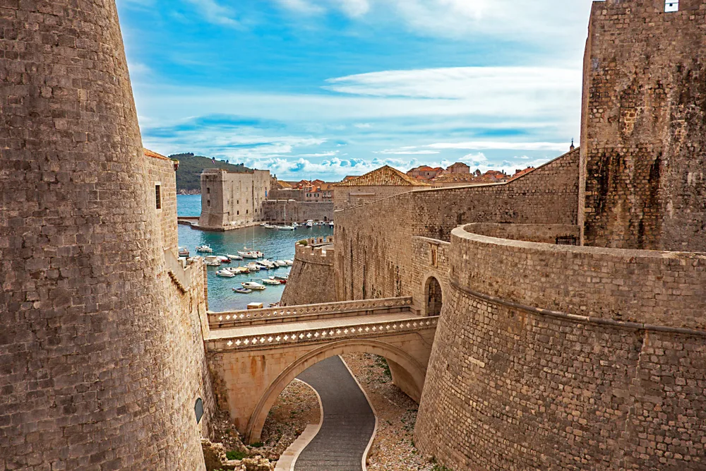 Photo of the old town harbor in Dubrovnik pictured with a stone bridge going over the walkway leading to the water