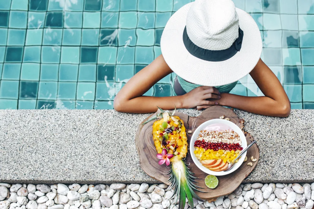 Woman eats fresh food by the pool on vacation to show how travel benefits health and wellness