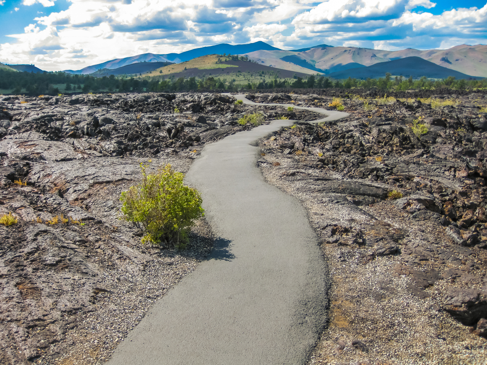Asphalt walkway winding through the Craters of the Moon Monument and Park, one of the best places to see in Idaho, with volcanic rock on either side