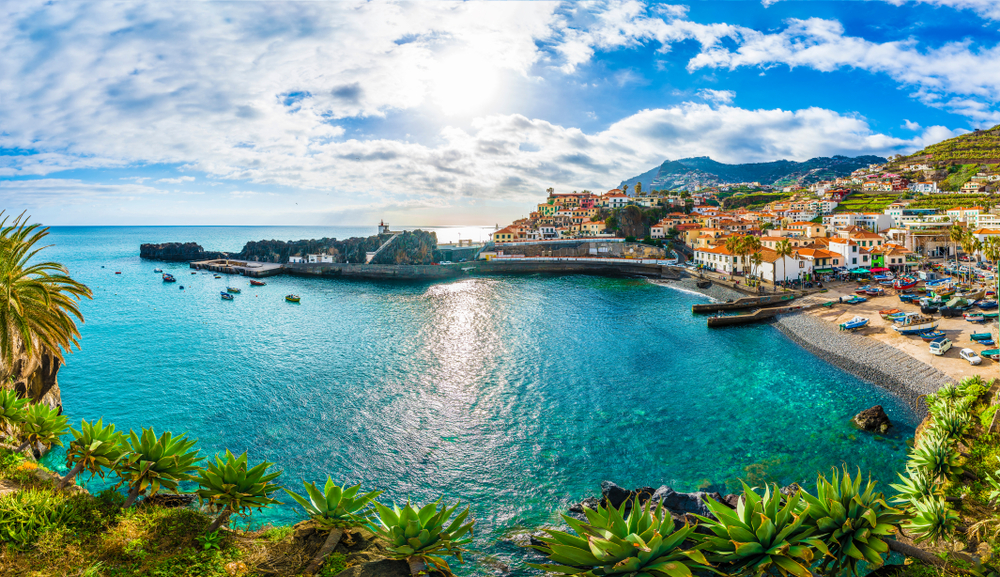The still bay surrounded by a rocky coast and vegetation with hilltop homes running up the steep island at Madeira, one of the best places to visit in Europe