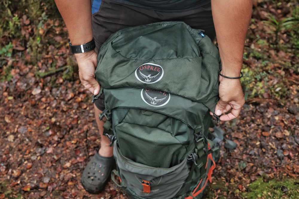 Man closes his green hiking pack outside with fallen leaves to show the concept of the best Osprey backpacks