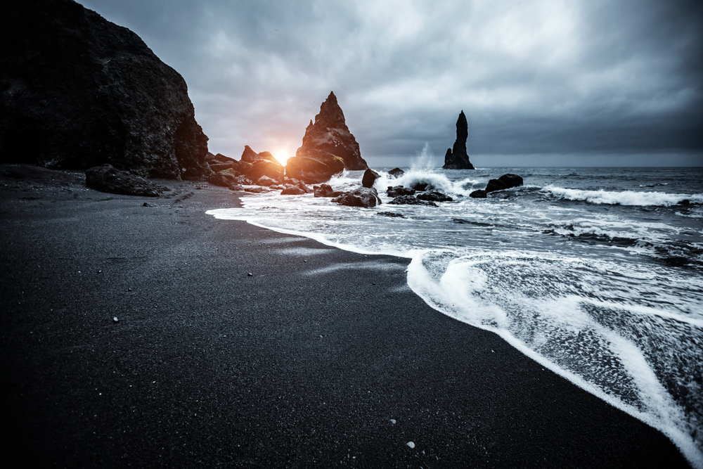Mystic bay in with rock formations jutting from the ocean, as seen from the Reynisfjara Beach, one of our top picks for the best places to visit in Iceland