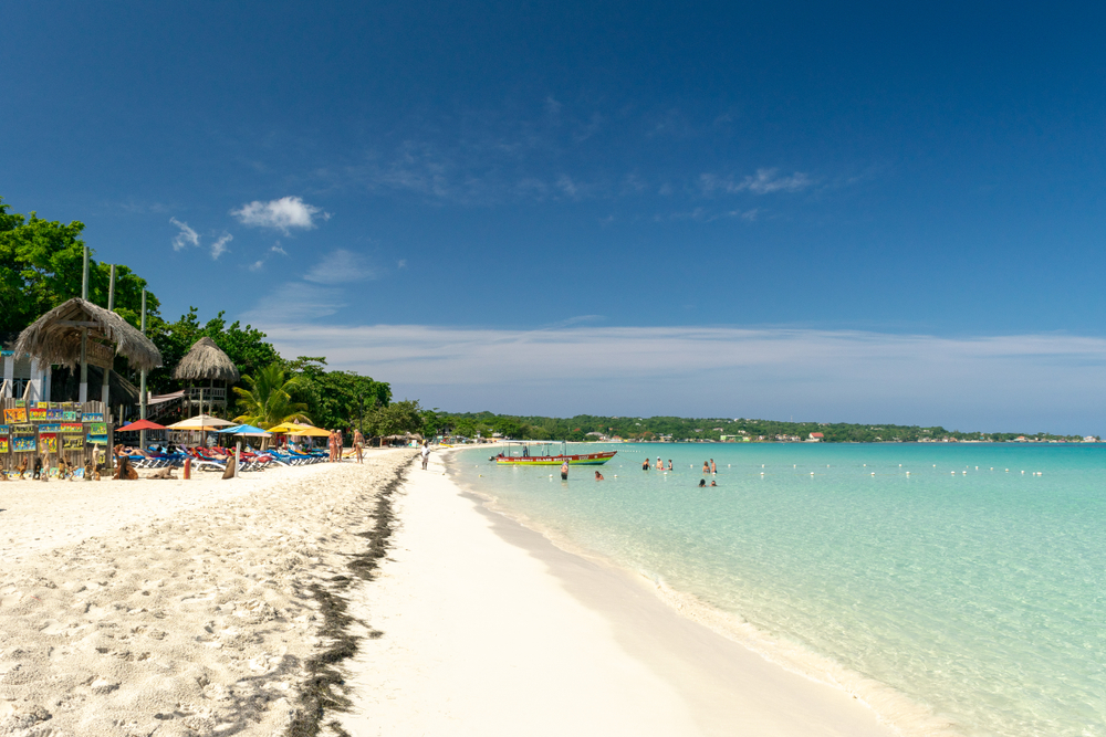 Tourists walking along the white sand beach of Negril for a piece on where to stay in Jamaica