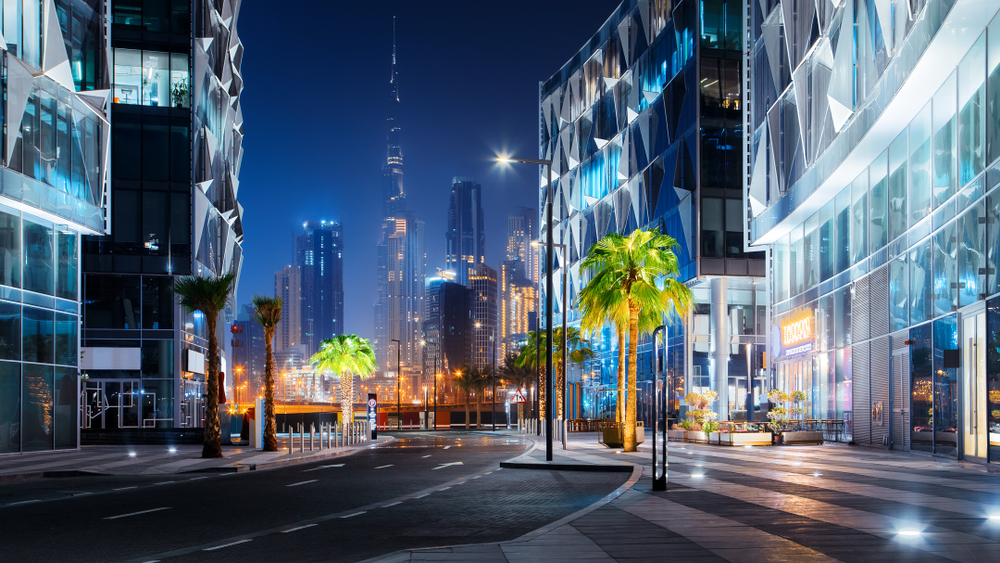 The beautiful downtown area pictured at night with amazing palm trees illuminated below modern high-rise buildings for a piece on where to stay in Dubai