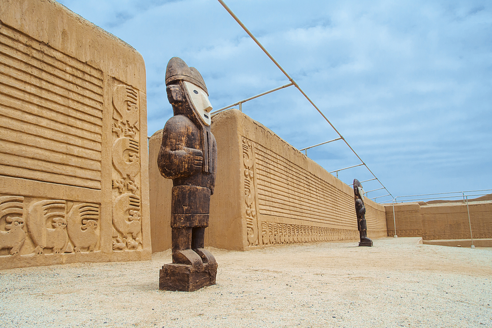 Wooden figures standing guard outside the entrance to Chan Chan, a must-visit place on a trip to Peru