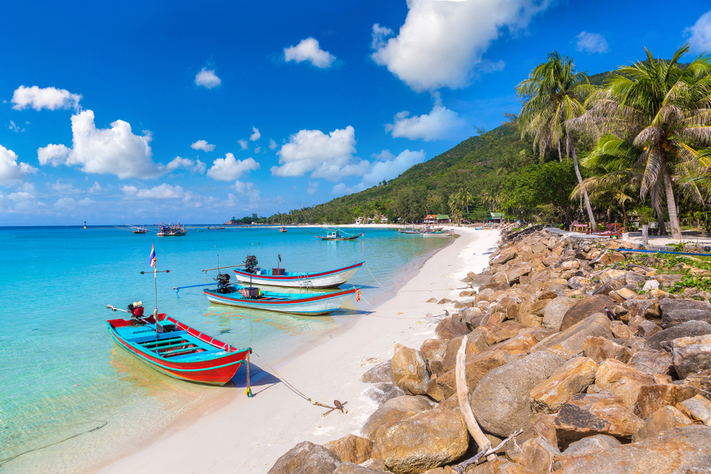 For a roundup of the best places to visit in Thailand, a few wooden boats in Koh Phangan float on the crystal-clear blue water