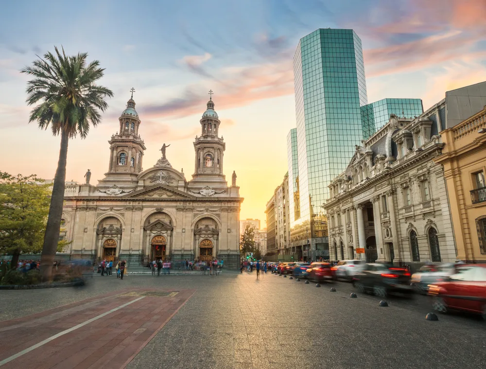 People in the Plaza de Armas Square in Santiago, one of the best places to visit in Chile, pictured with the sun setting over the downtown buildings