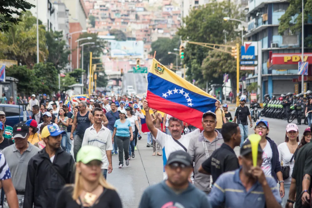 Protests in Caracas pictured with people walking through the streets holding signs and flags
