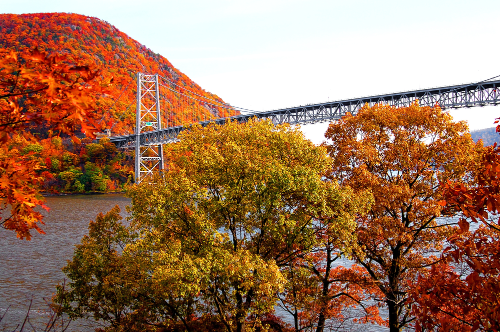 For a roundup of the best day trips from New York City, a metal bridge spans the river in the fall with red leaves in full view
