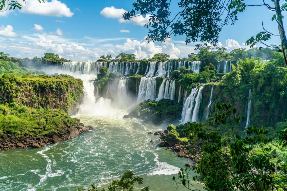 View of the stunning Iguazu Falls in Argentina as seen on a clear day from between the trees, from the perspective of a person standing on a viewing platform