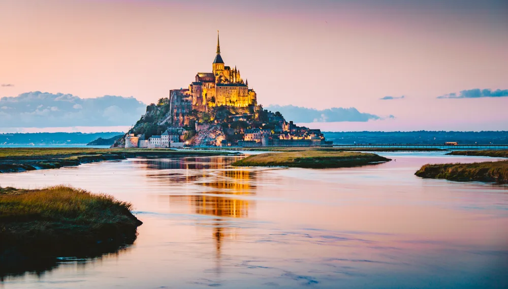 Stunning view of Mont-Saint-Michel, one of the best day trips from Paris, pictured sitting on its giant rock overlooking the water at low tide