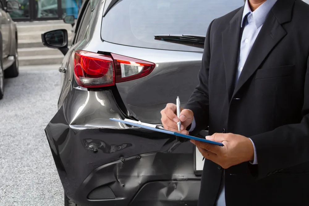 Man holding clipboard surveys damage to rental car for a piece asking should you get insurance for a rental car