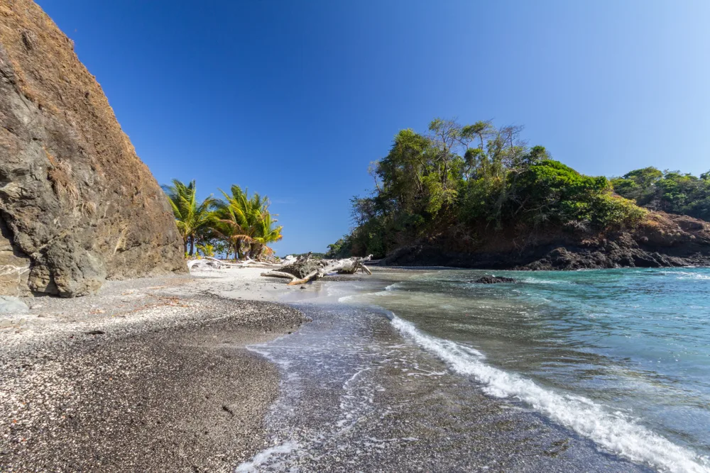 Las Perlas, one of the best places to visit in Panama, pictured with a gorgeous black-sand beach between two rock formations with vegetation on both