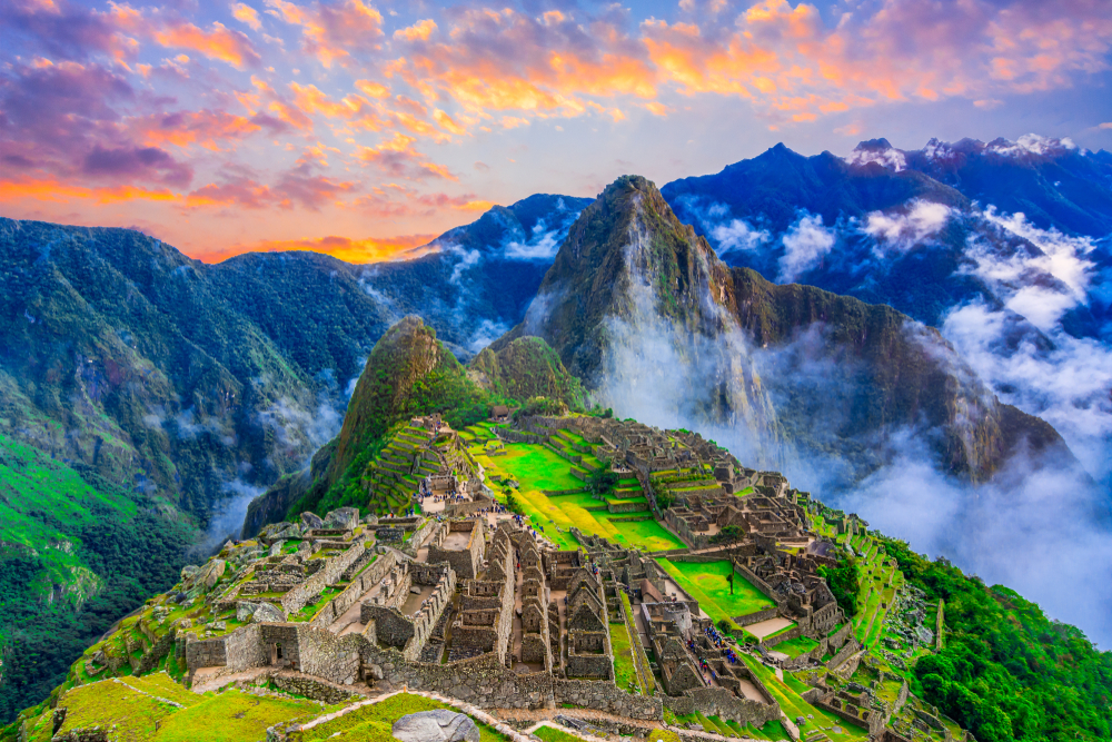 Ruins of the mountain-top town of Machu Picchu with the sun setting over the mountains and clouds in the valley below