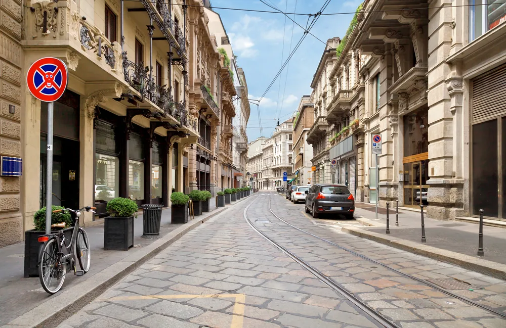For a piece titled Where to Stay in Milan, the historic area of Centro Storico is pictured with brick buildings on either side of the road and its tracks