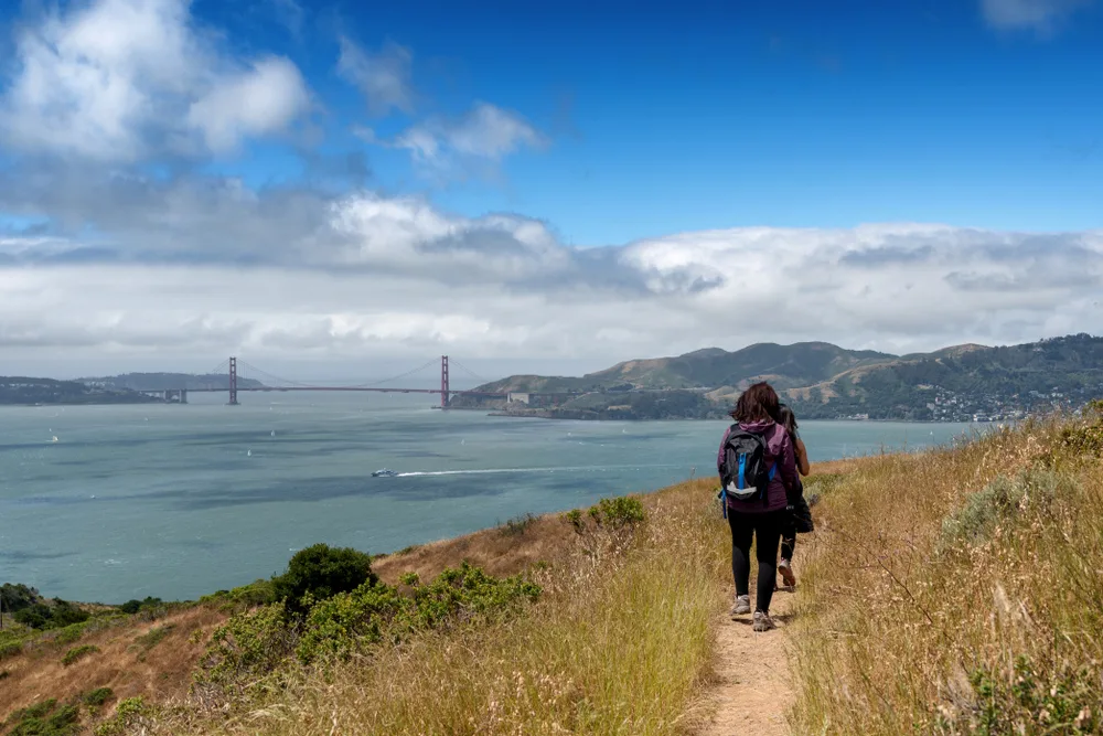 Hikers on Angel Island, a great day trip from San Francisco, pictured in the fall with a boat driving by on the water below