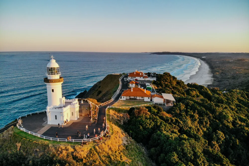 Hilltop lighthouse pictured high above Byron Bay, one of Australia's best areas to visit, on a clear day with a peach-colored sky