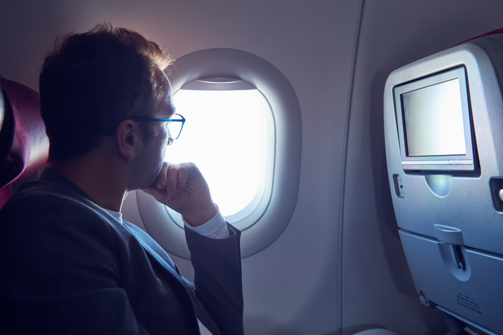 Man looks out airplane window with hand under his chin for a piece posing the question how safe is flying